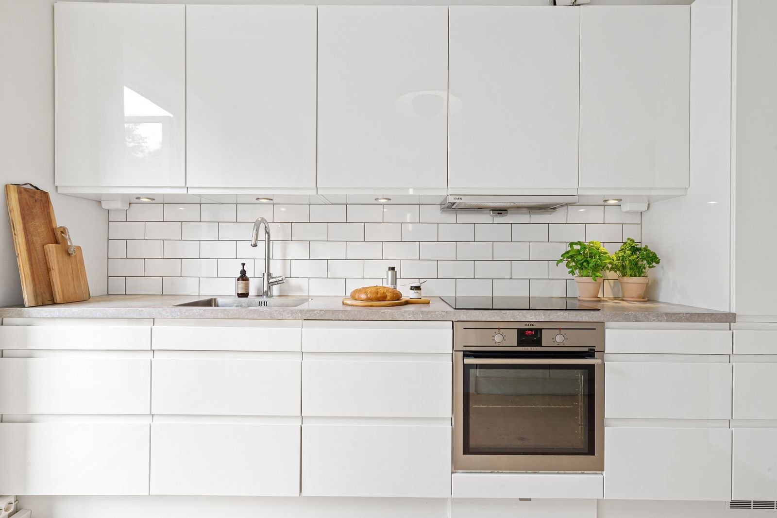 Sleek white kitchen with subway tiles, a built-in oven and herbs.