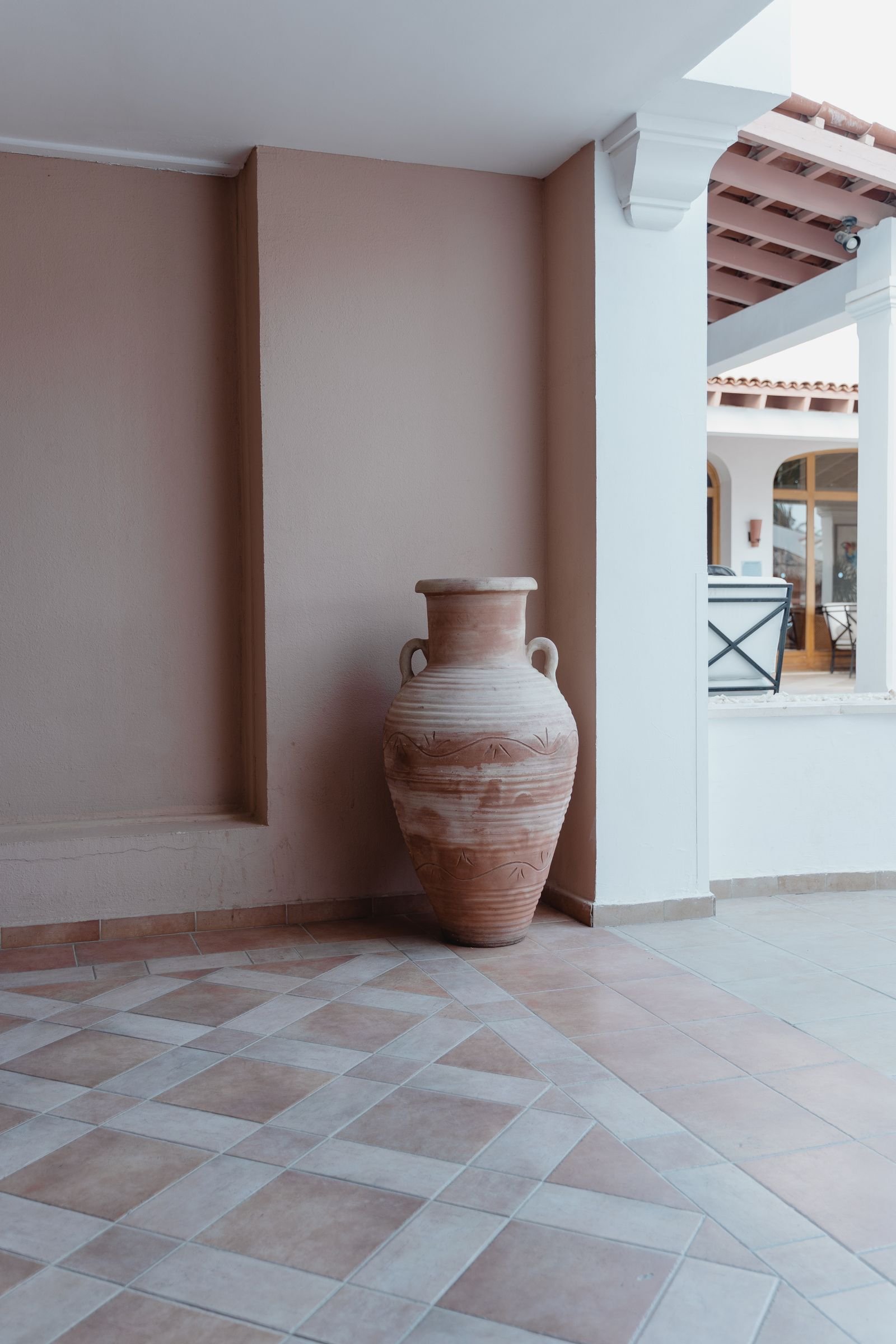 Large clay amphora in a tiled interior corner with neutral walls.
