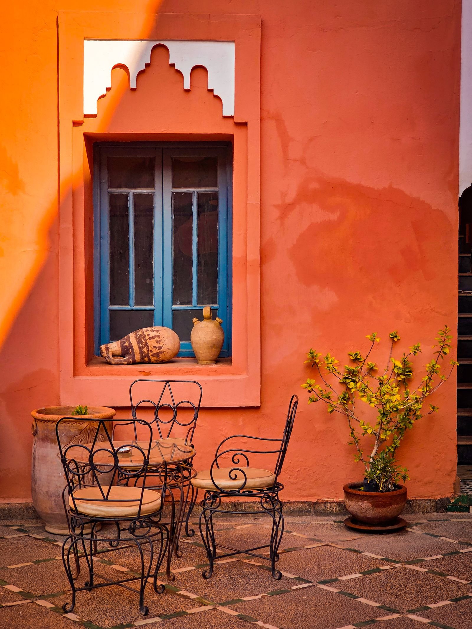 Patio with iron chairs, terracotta pots and an orange wall.