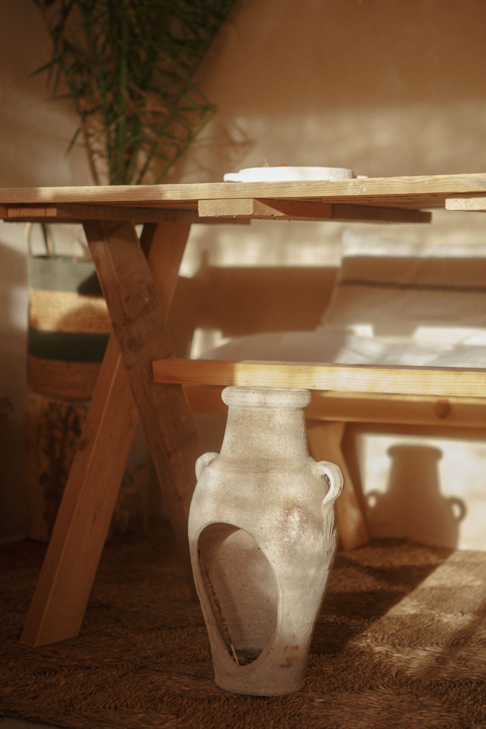 Warm Mediterranean room with a rustic table, vase and soft sunlight.