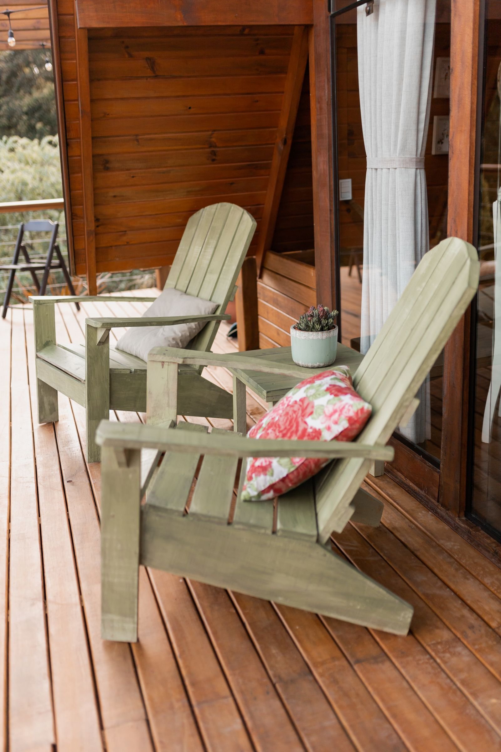 Wooden deck with Adirondack chairs and a potted plant.