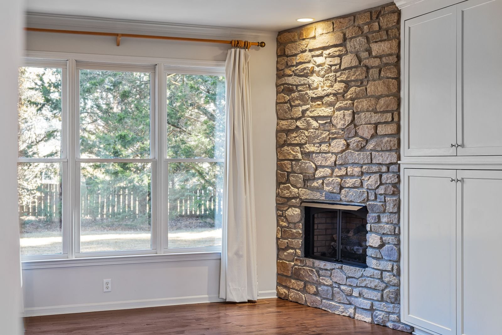 Bright modern living room with a stone fireplace wall and large windows.