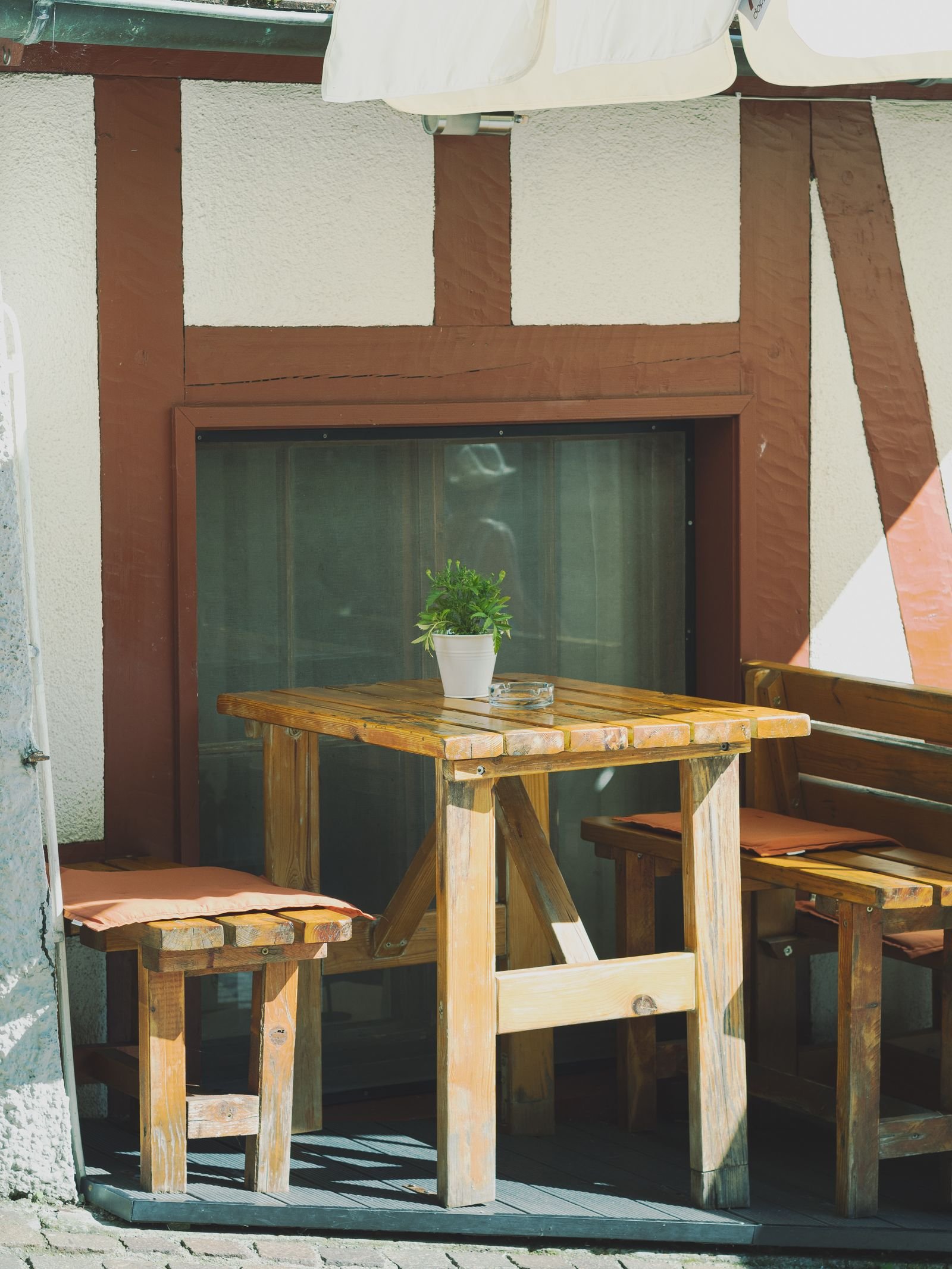 Rustic patio with a wooden table, chairs and a potted plant.