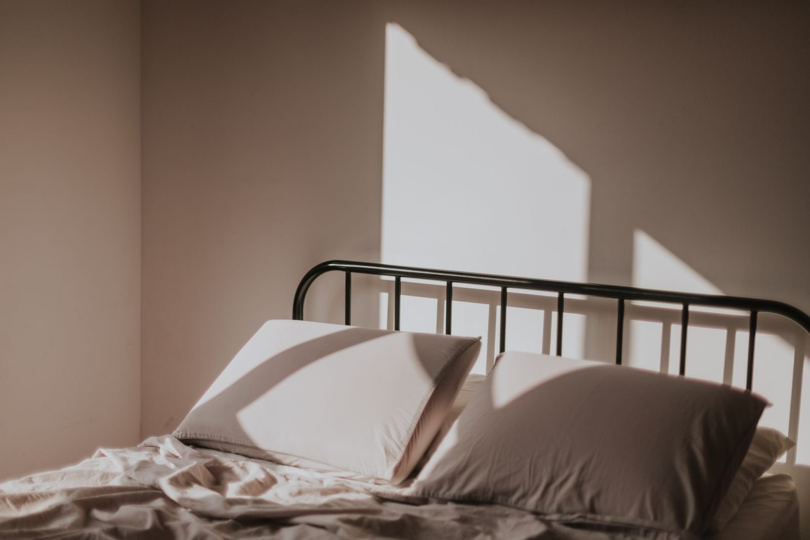 Soft morning light falling on a neatly made bed with a metal headboard.