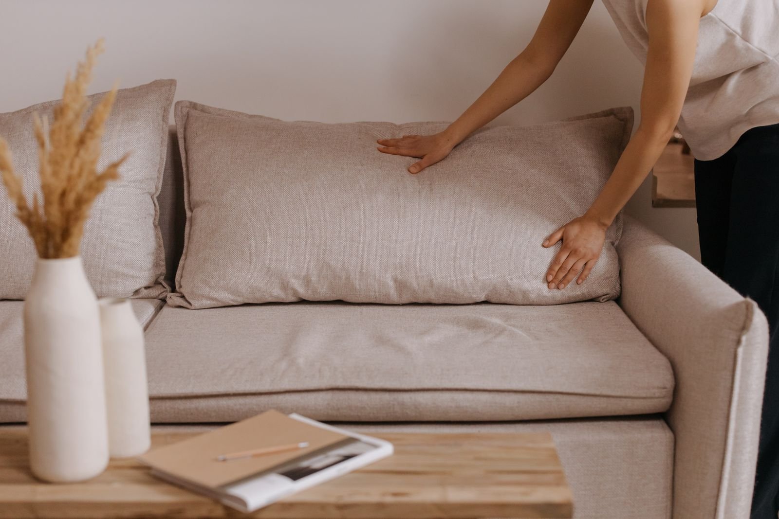 Person arranging a pillow on a beige sofa in a minimalist living room.