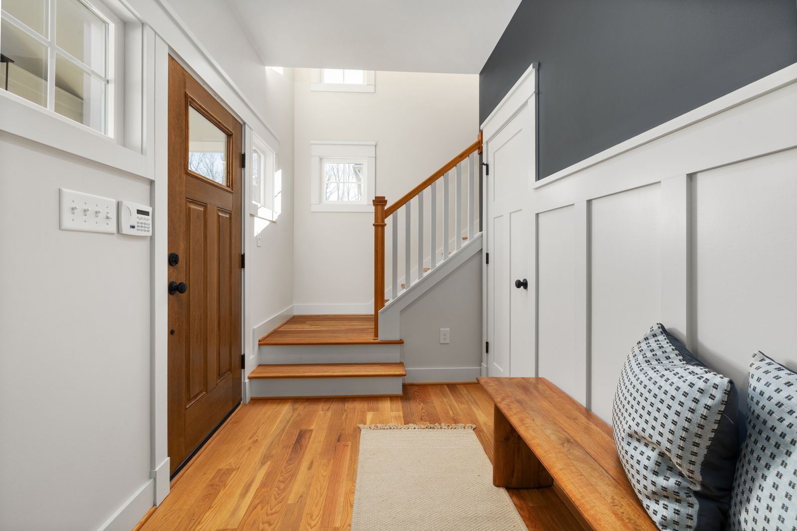 Bright entryway with wooden flooring, a bench and natural light.