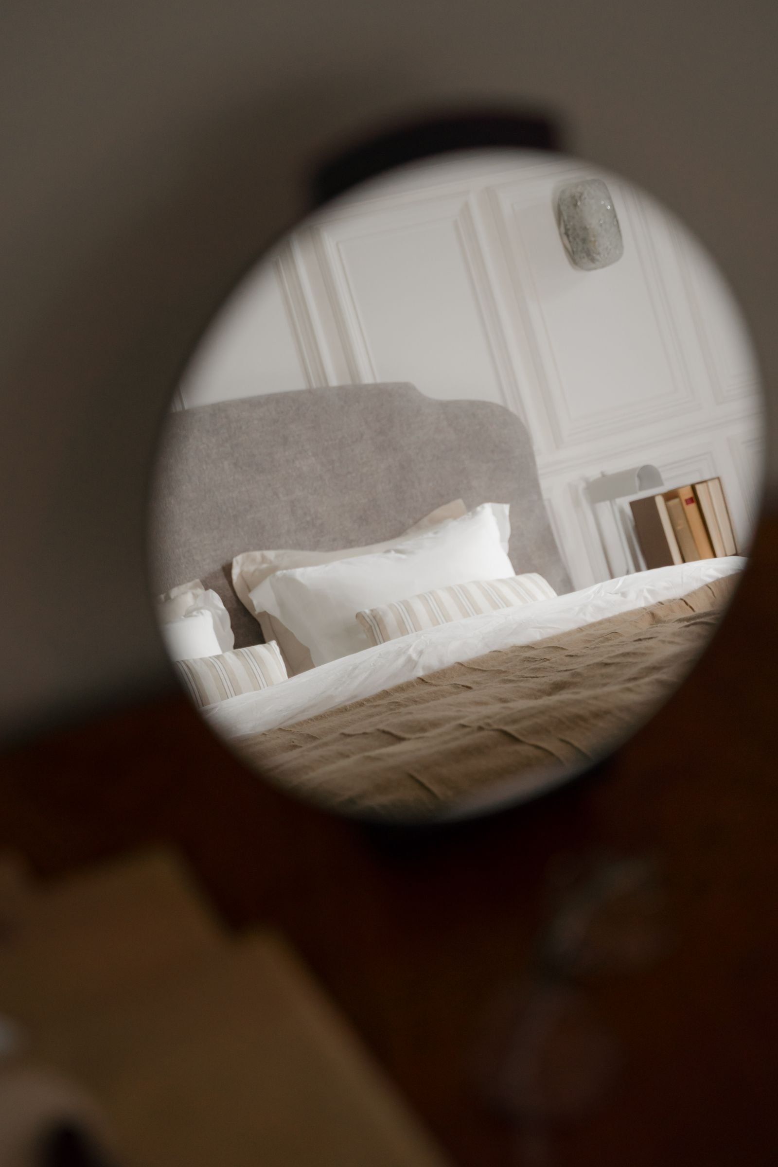 Cozy modern bedroom with a made bed reflected in a round mirror.