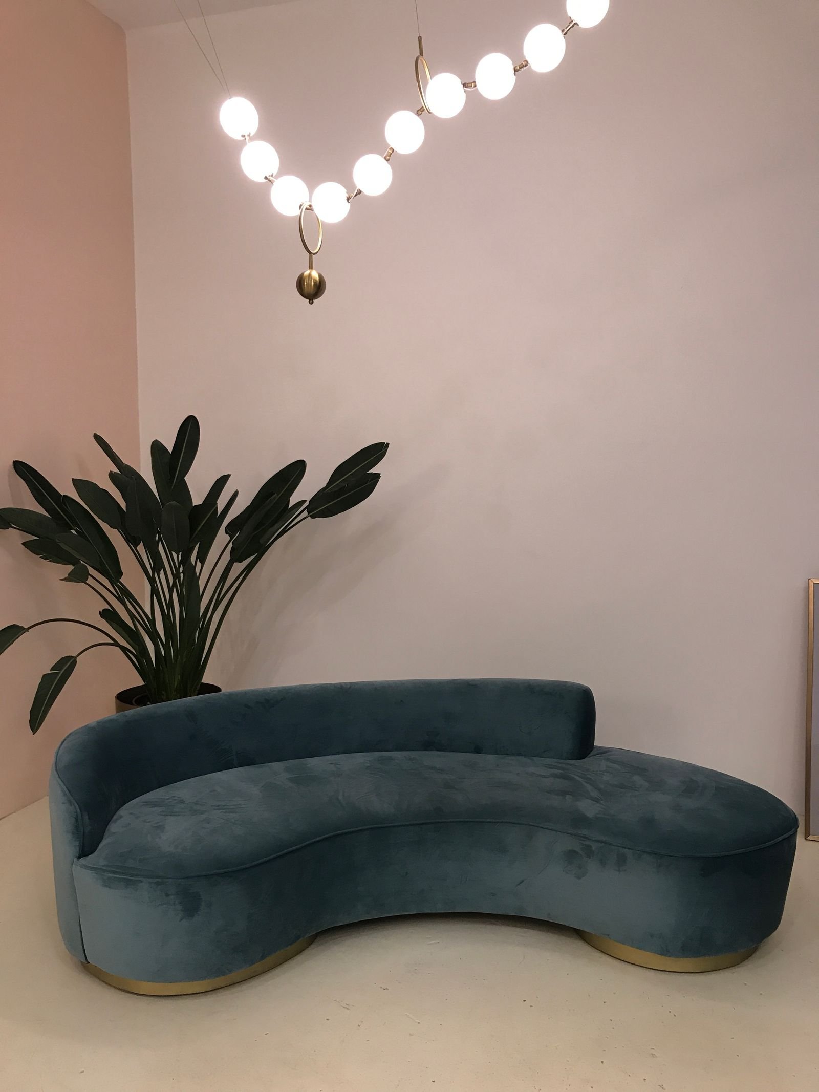 Teal curved sofa beside a green plant and hanging lights in a living room.