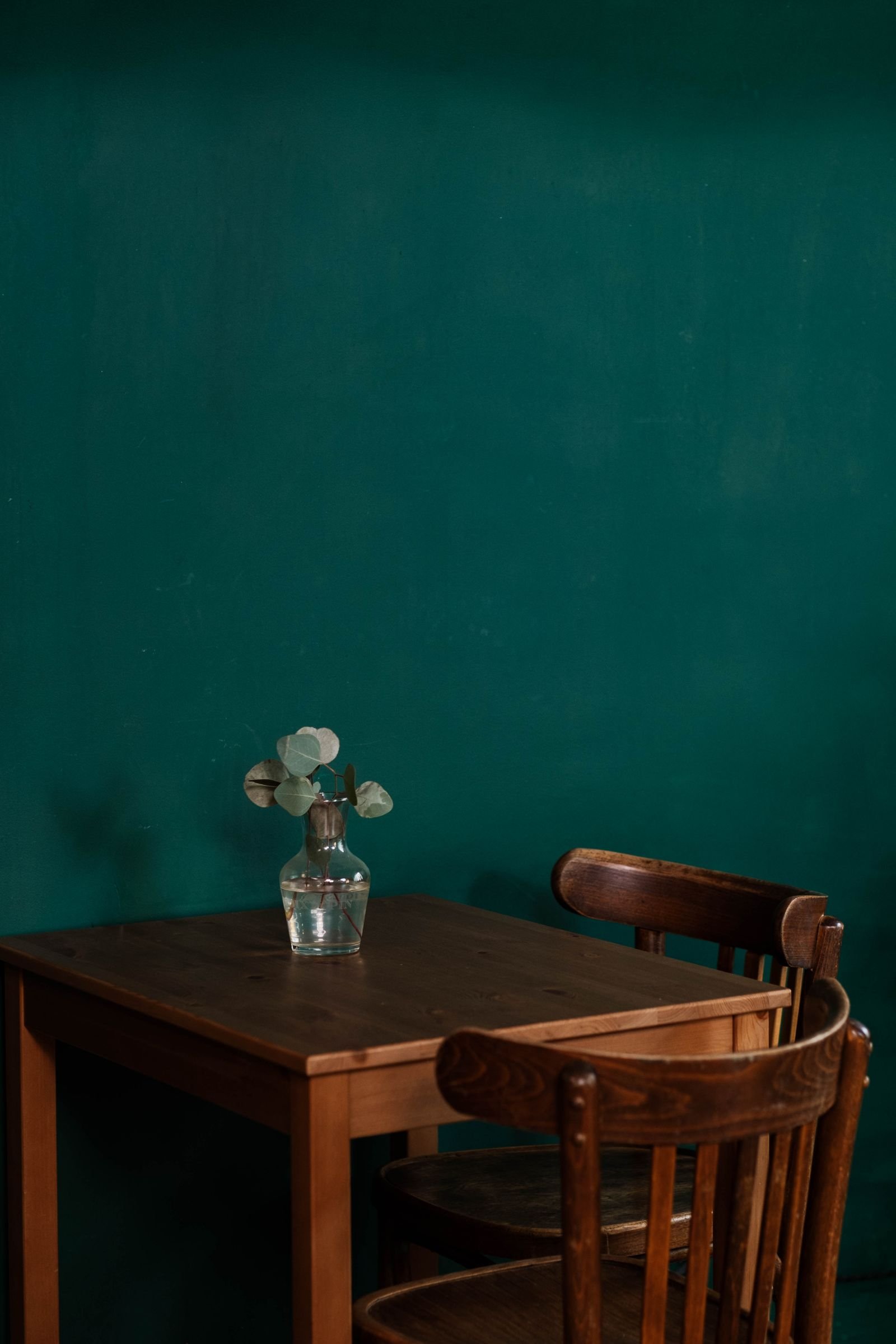 Vase with foliage on a wooden table in front of a teal wall.