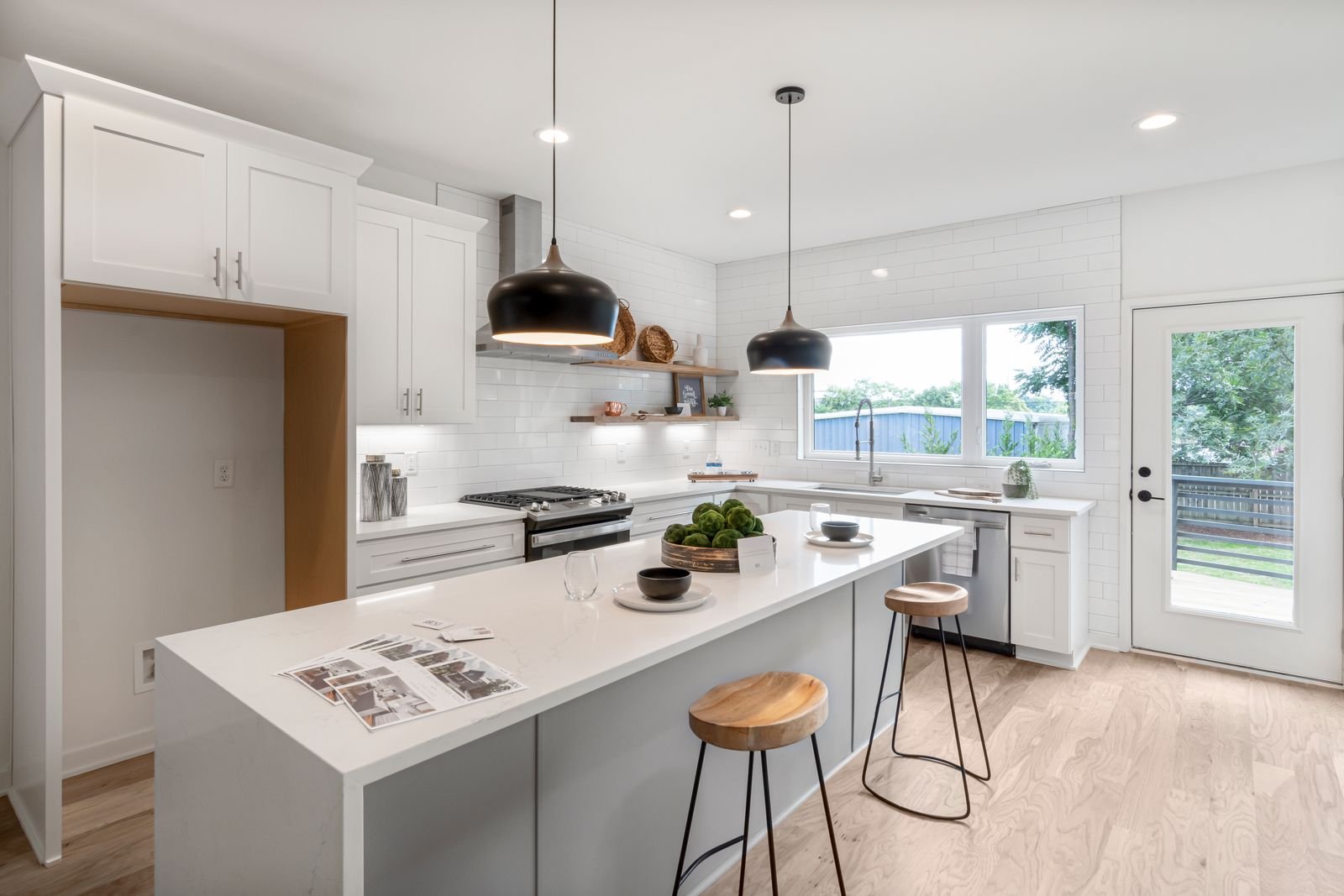 Bright white kitchen with wooden stools and pendant lights.