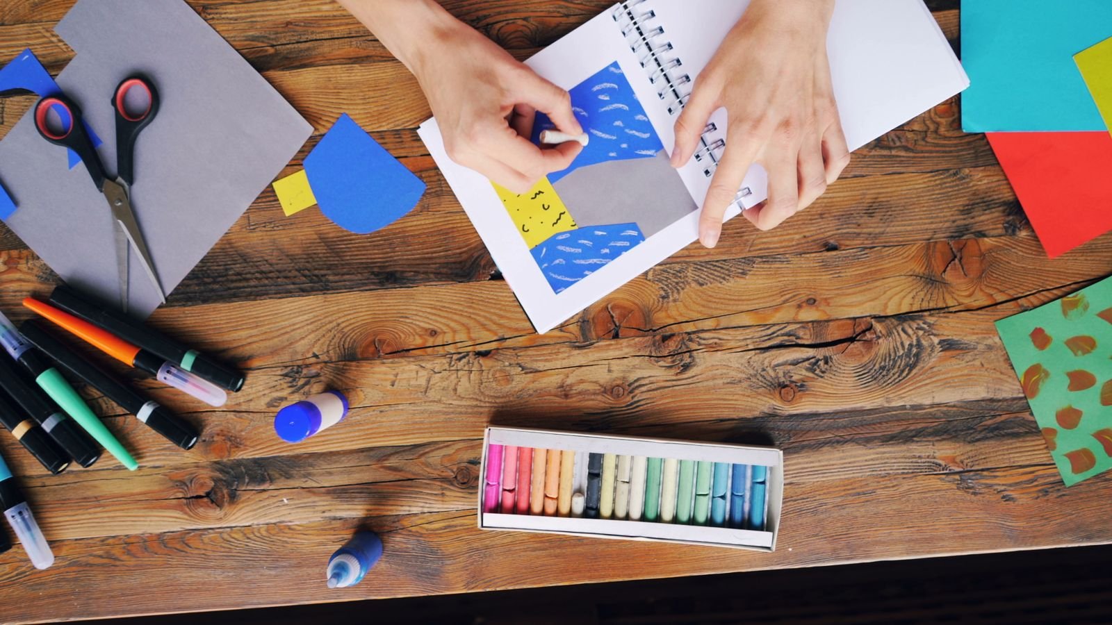 Colorful papers in pastel shades laid out for a craft project on a wooden table.
