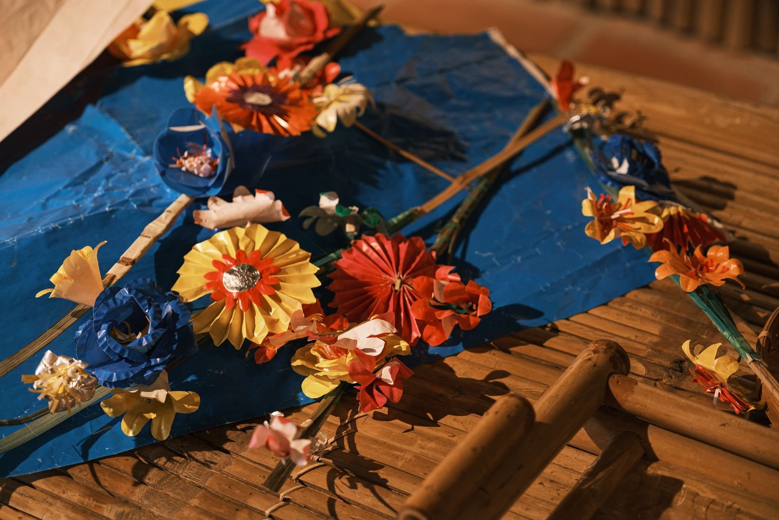 Handmade paper flowers in bright colors arranged on a bamboo surface.