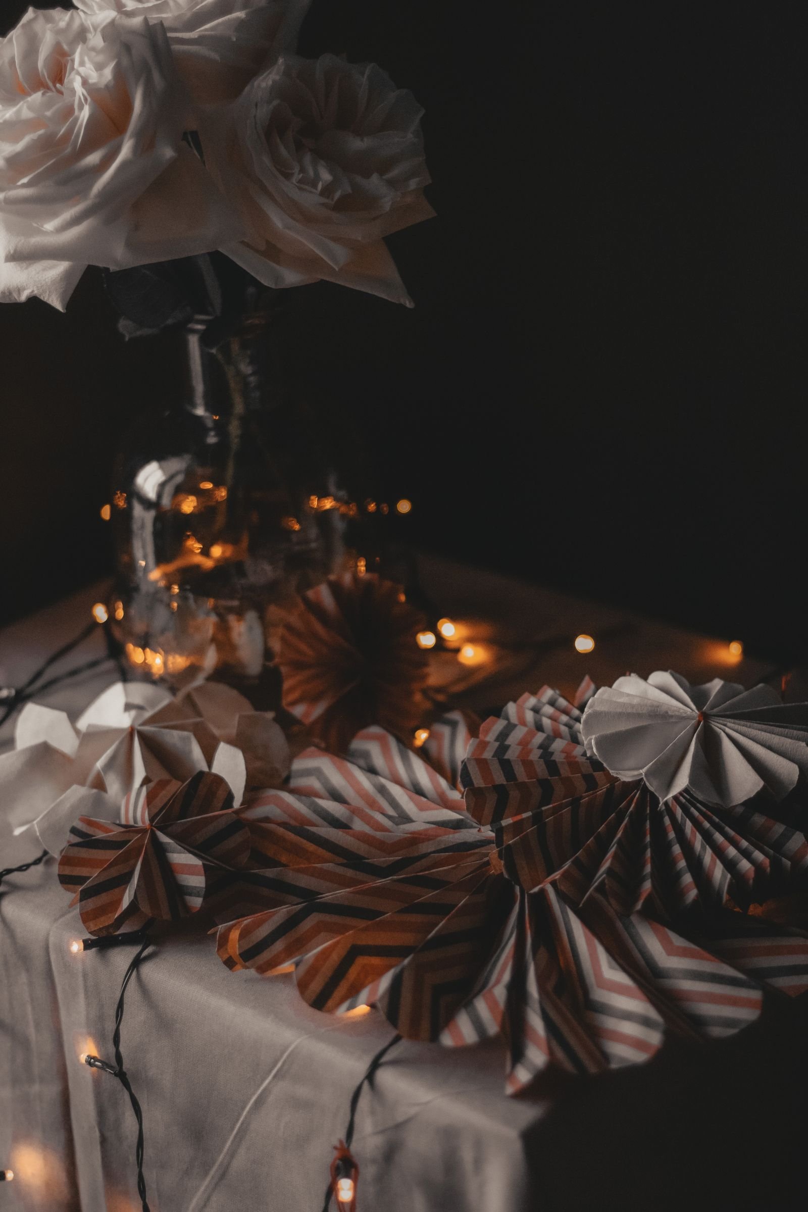 Handmade paper decorations and a glowing garland on a table with flowers.