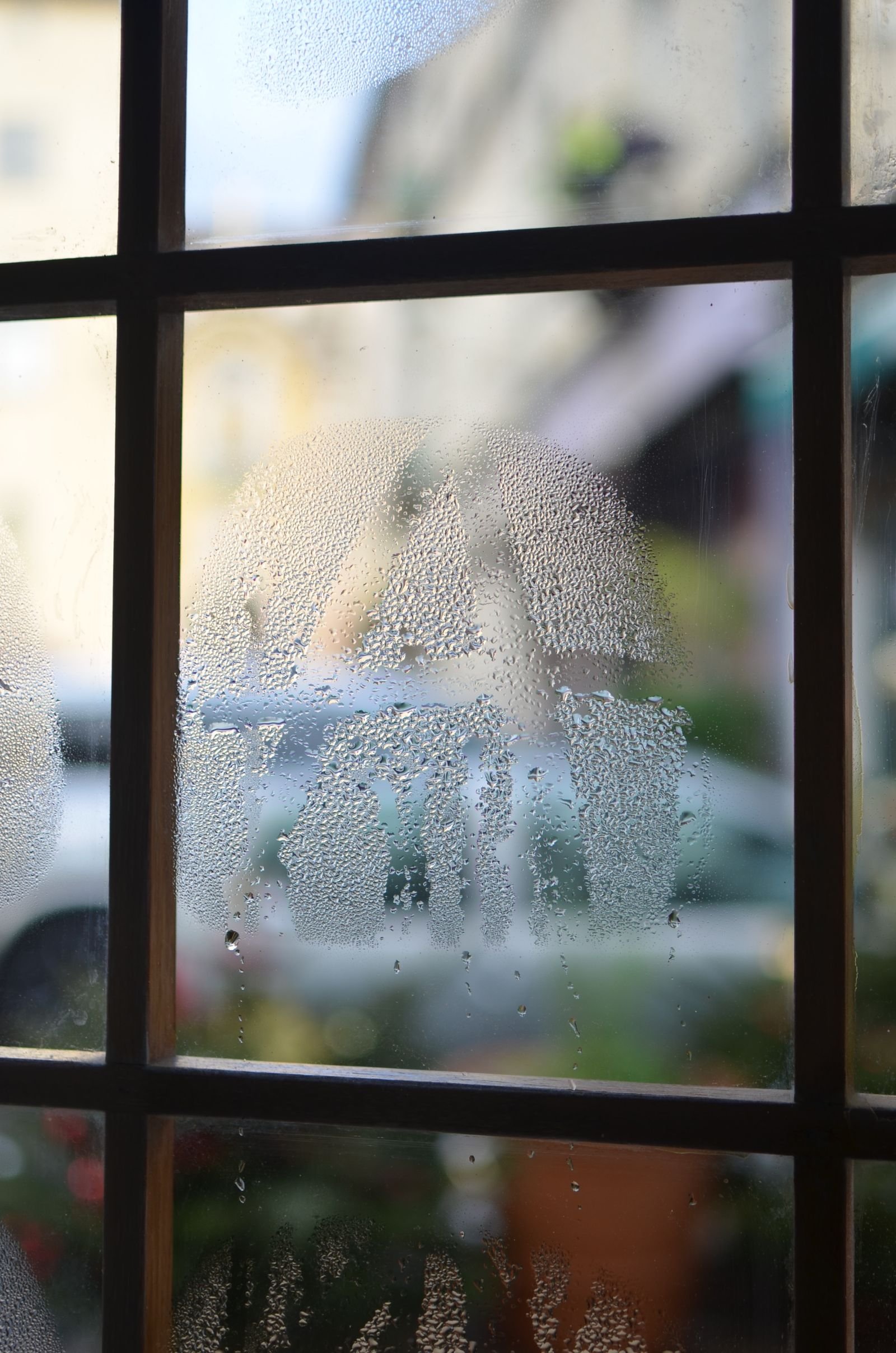 Misted window glass with small water drips running down the pane.