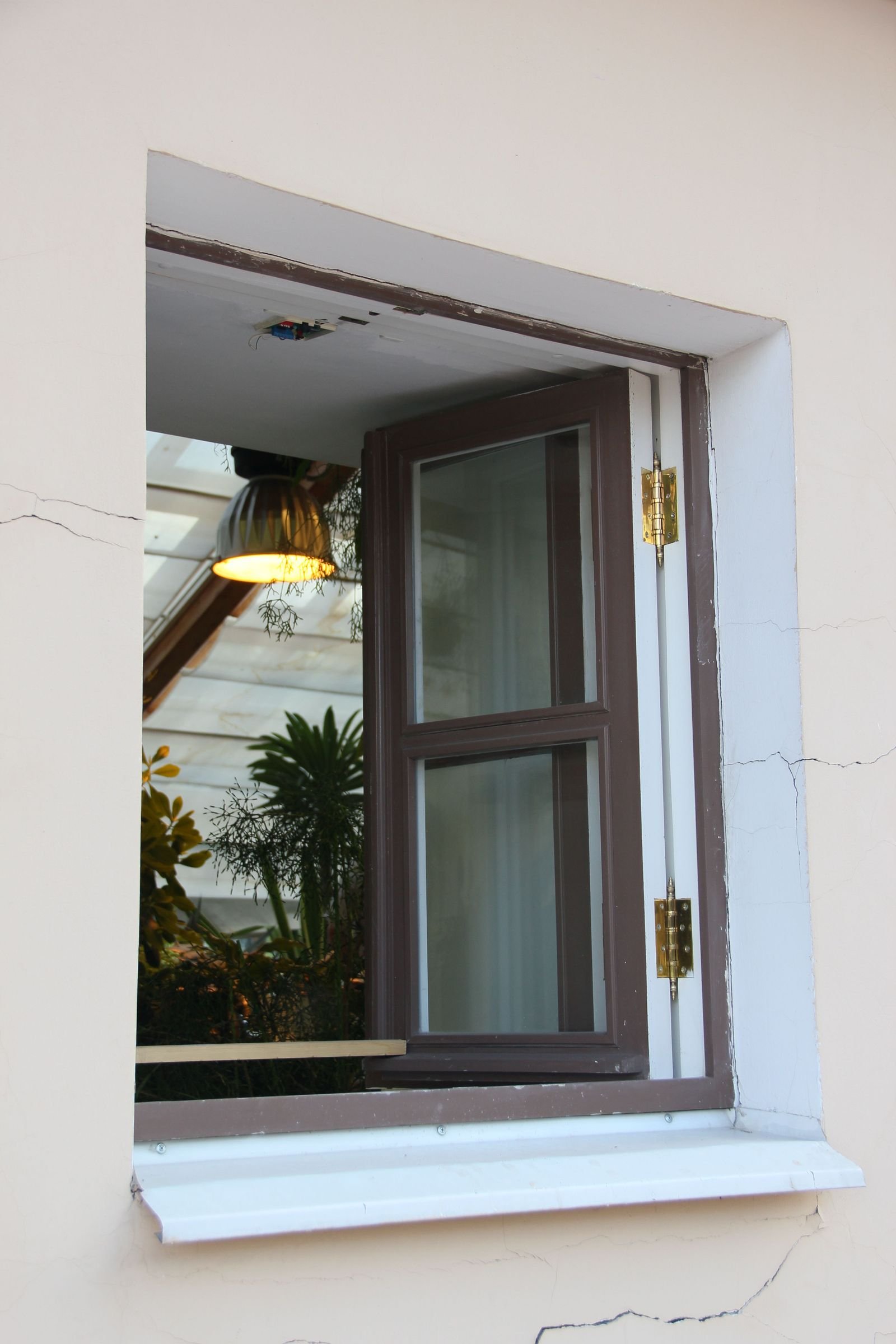 Open brown-framed window with indoor plants and soft light inside.
