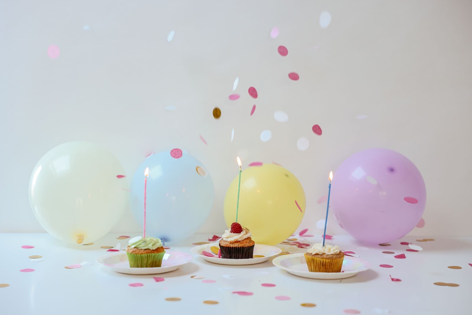 Cupcakes with candles, balloons and confetti on a table.