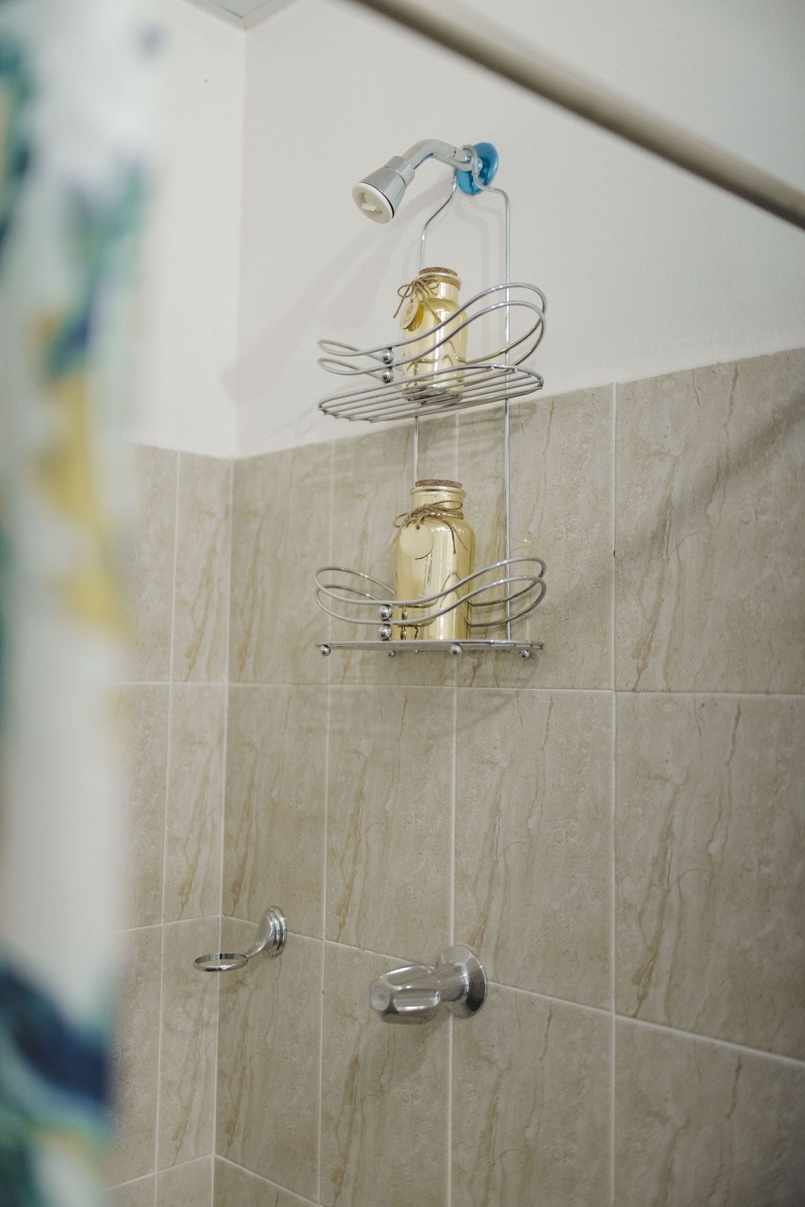 Shower with a wire shelf of jars against a tiled wall.
