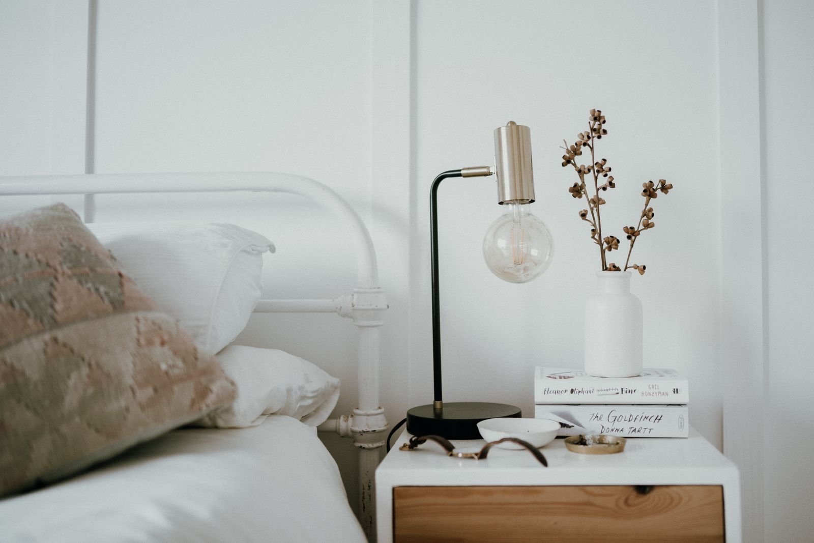 Bedside table with a lamp, books and small decor in a minimalist bedroom.
