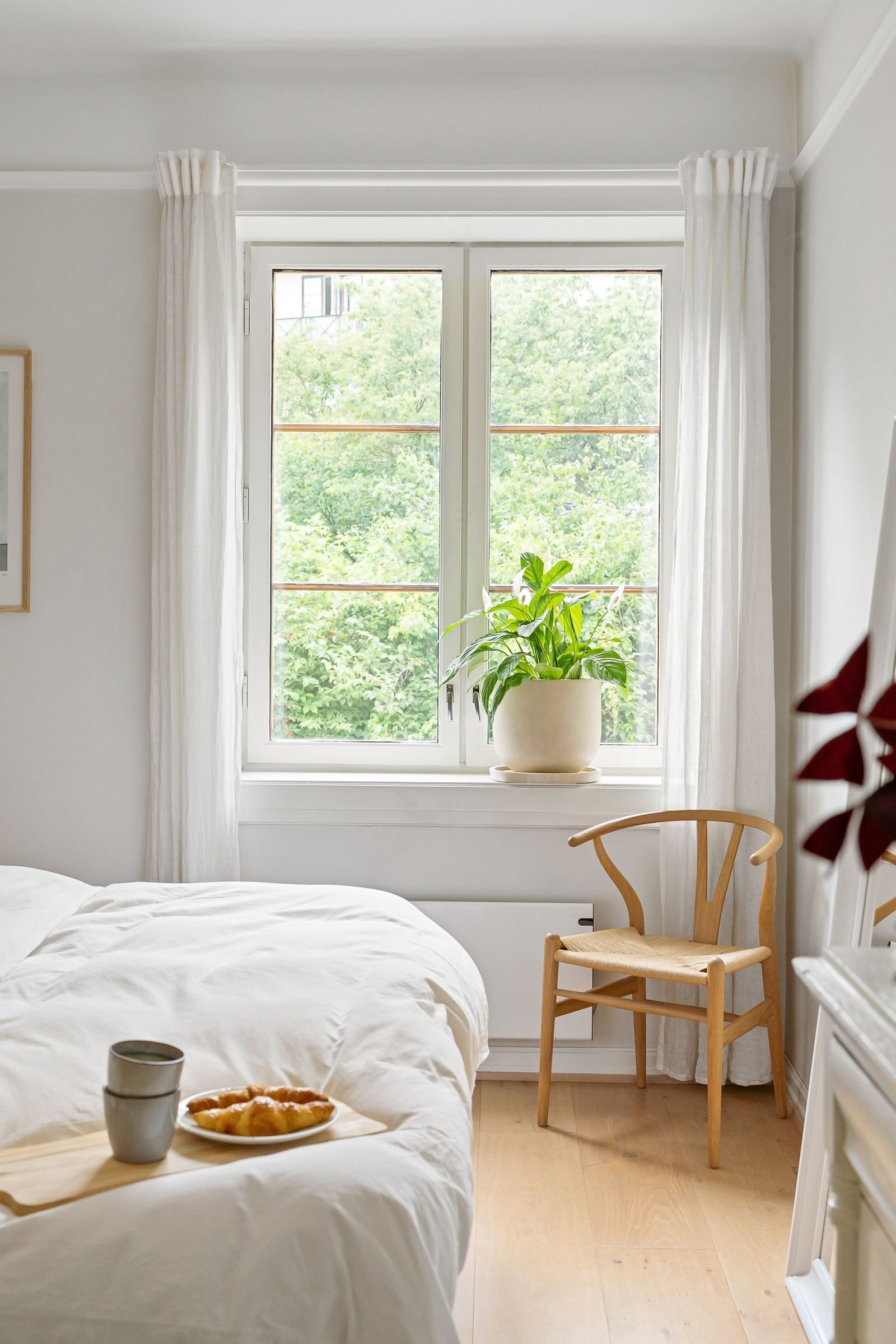 Bright bedroom with a window, a wooden chair and green plants.