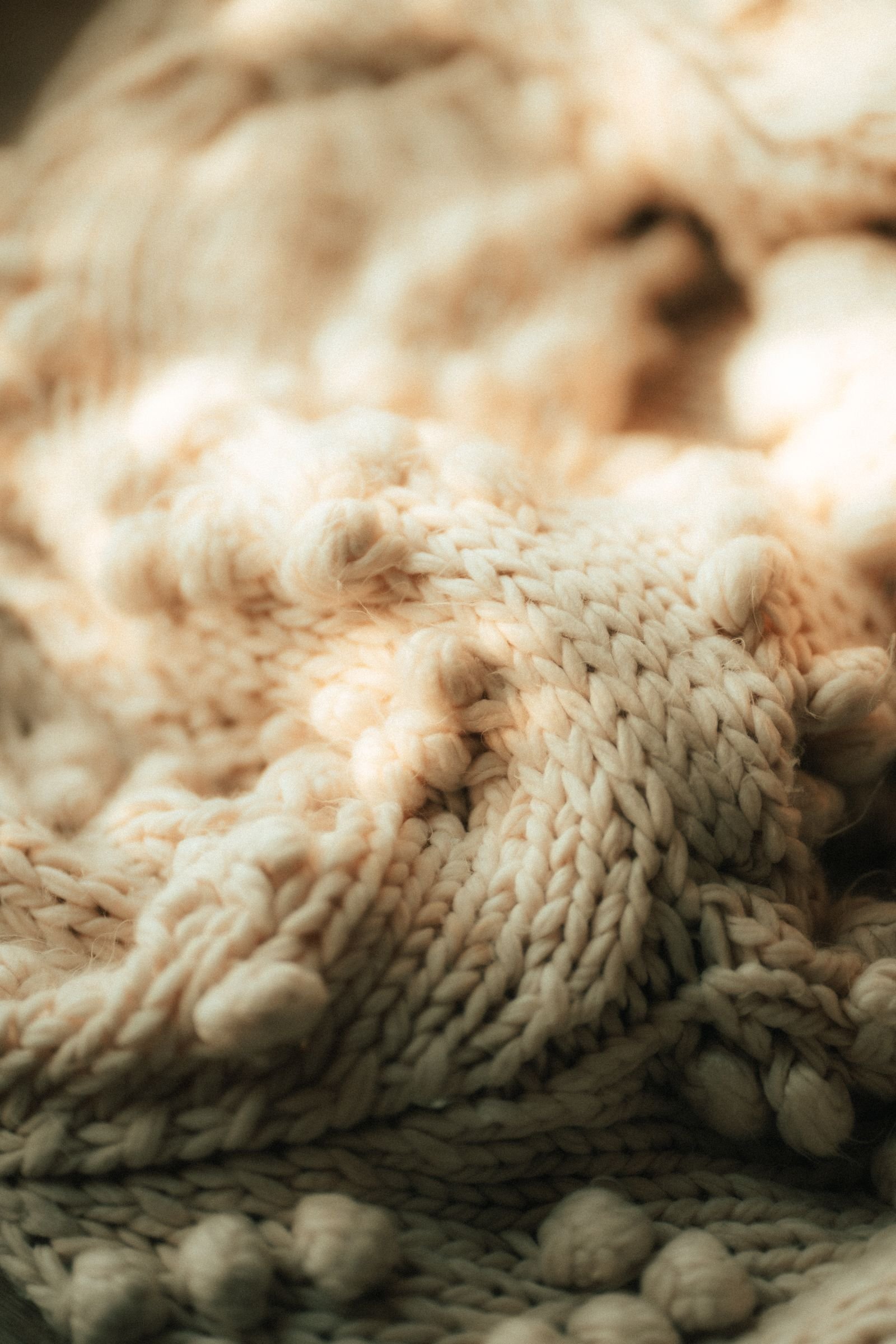 Beige knitted blanket with pom-poms in soft light.