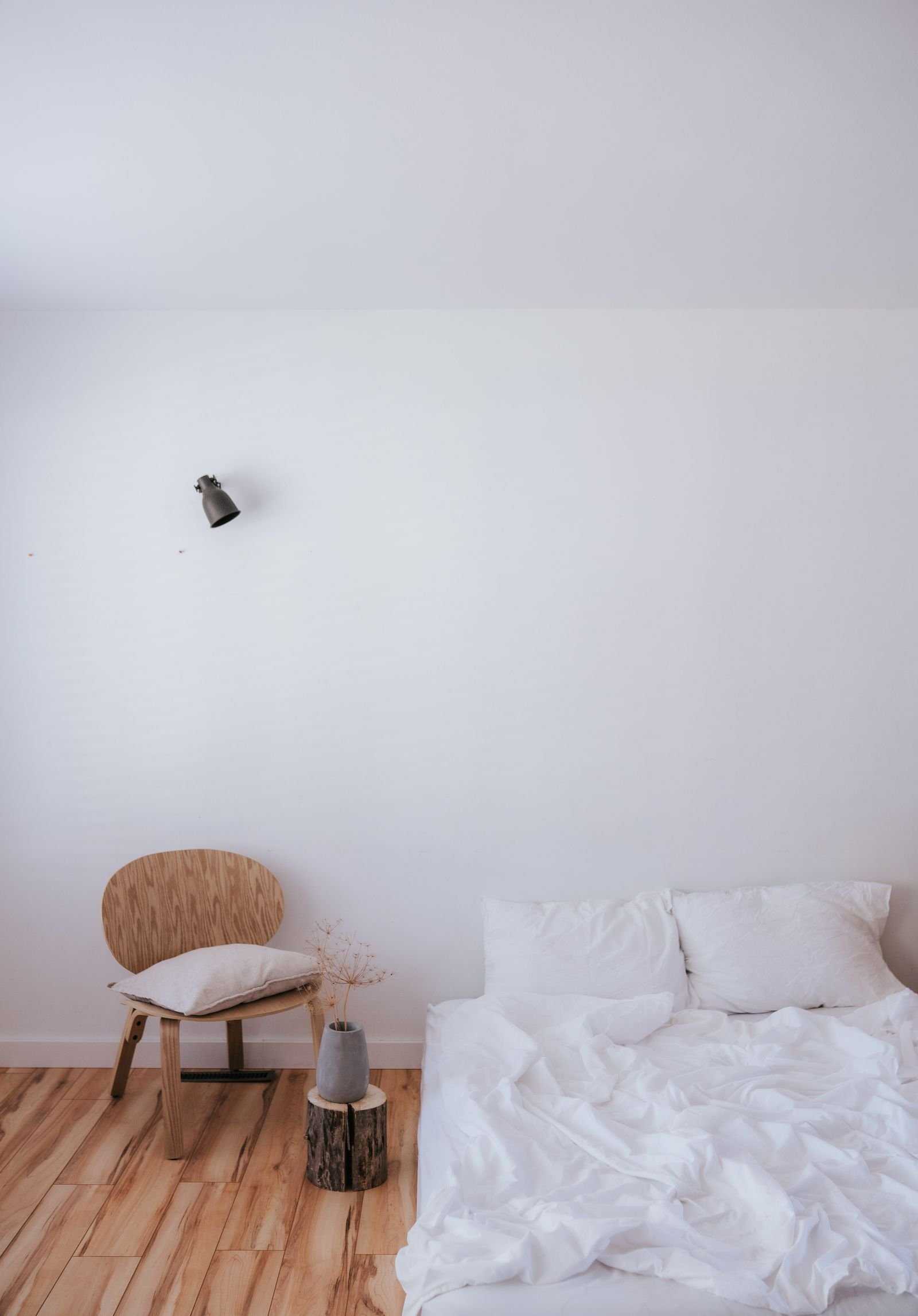 Minimalist bedroom with a white bed and a wooden chair.