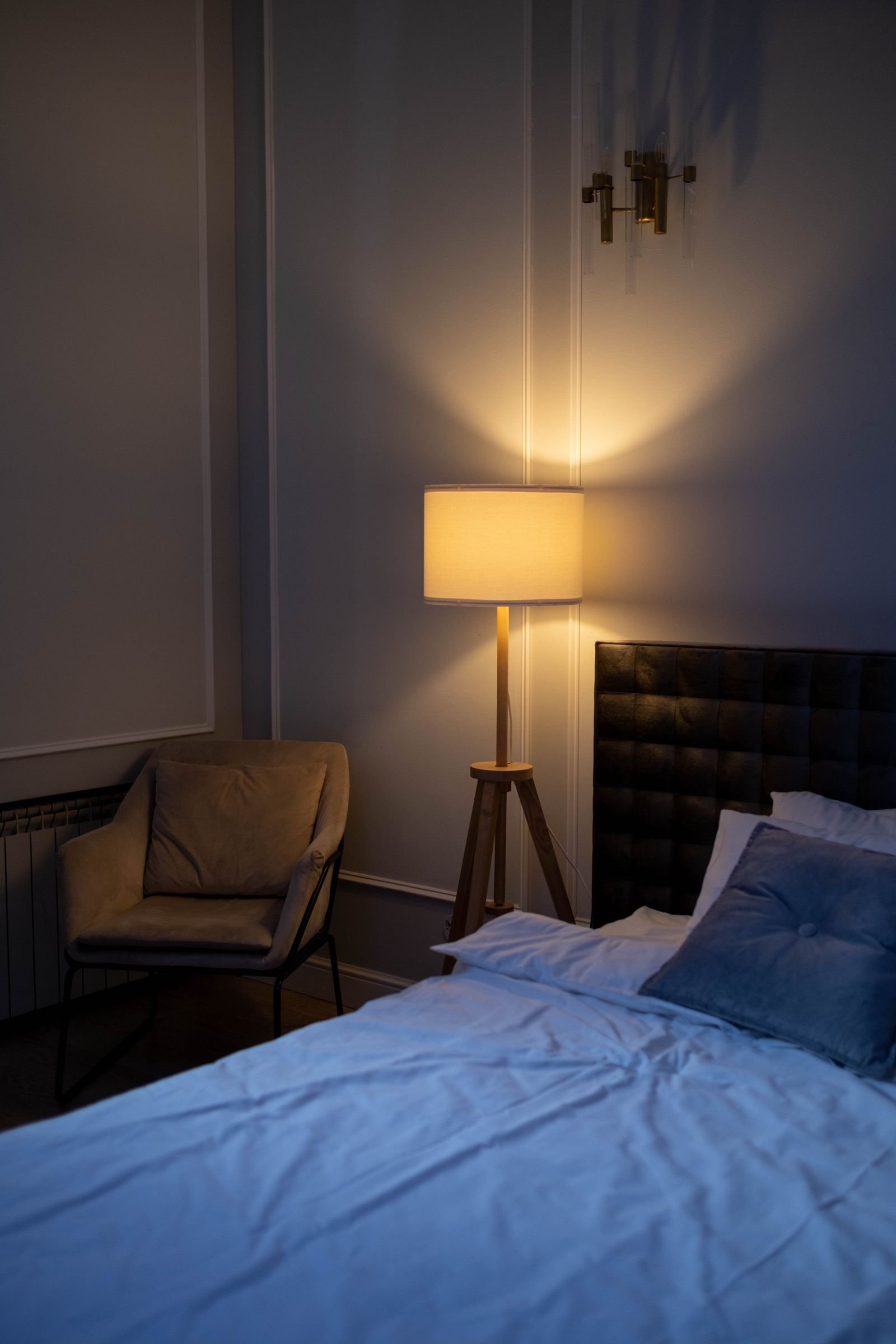 Bedroom with a made bed, an armchair and a floor lamp.