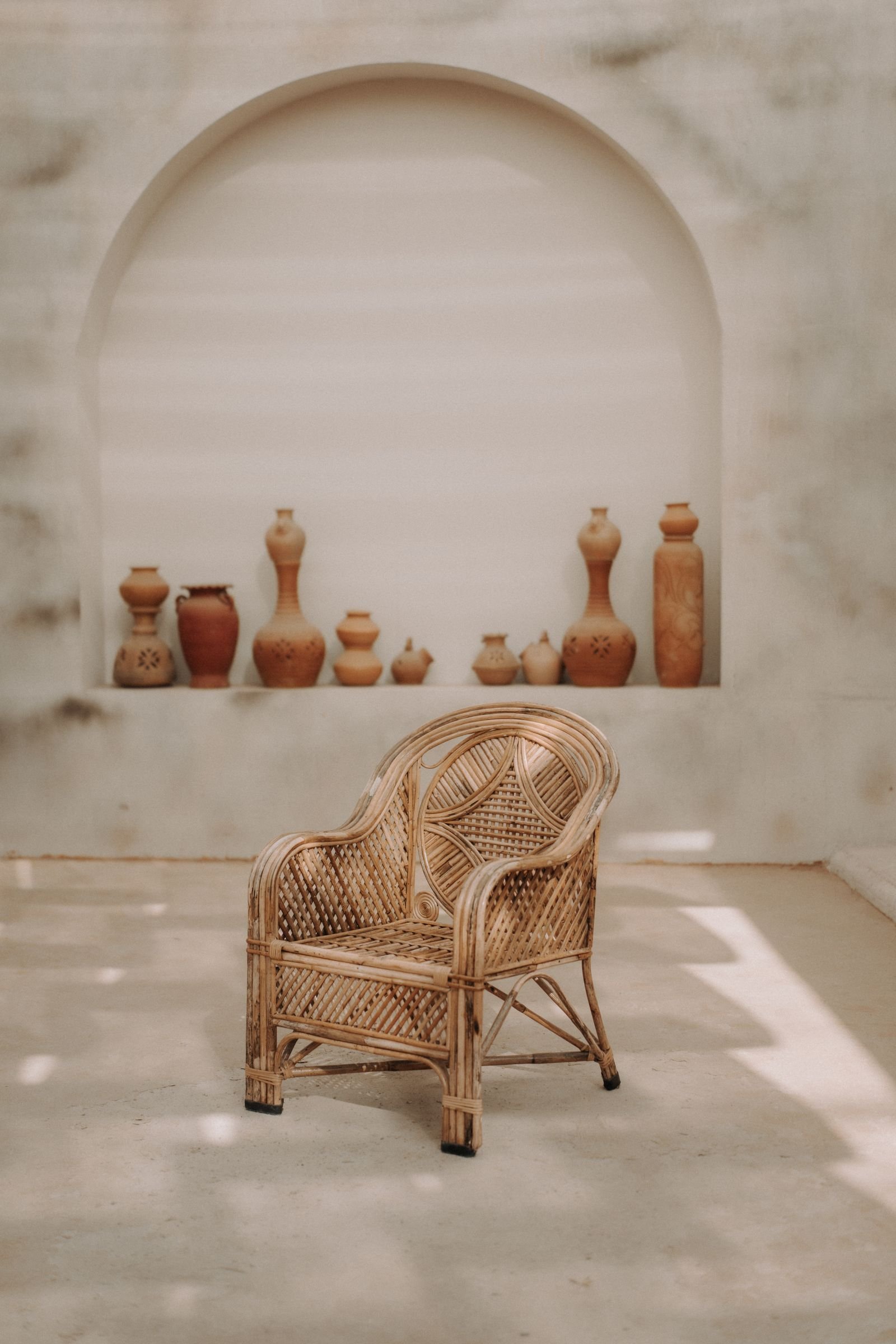 Wicker armchair beside clay vases in a minimalist room.