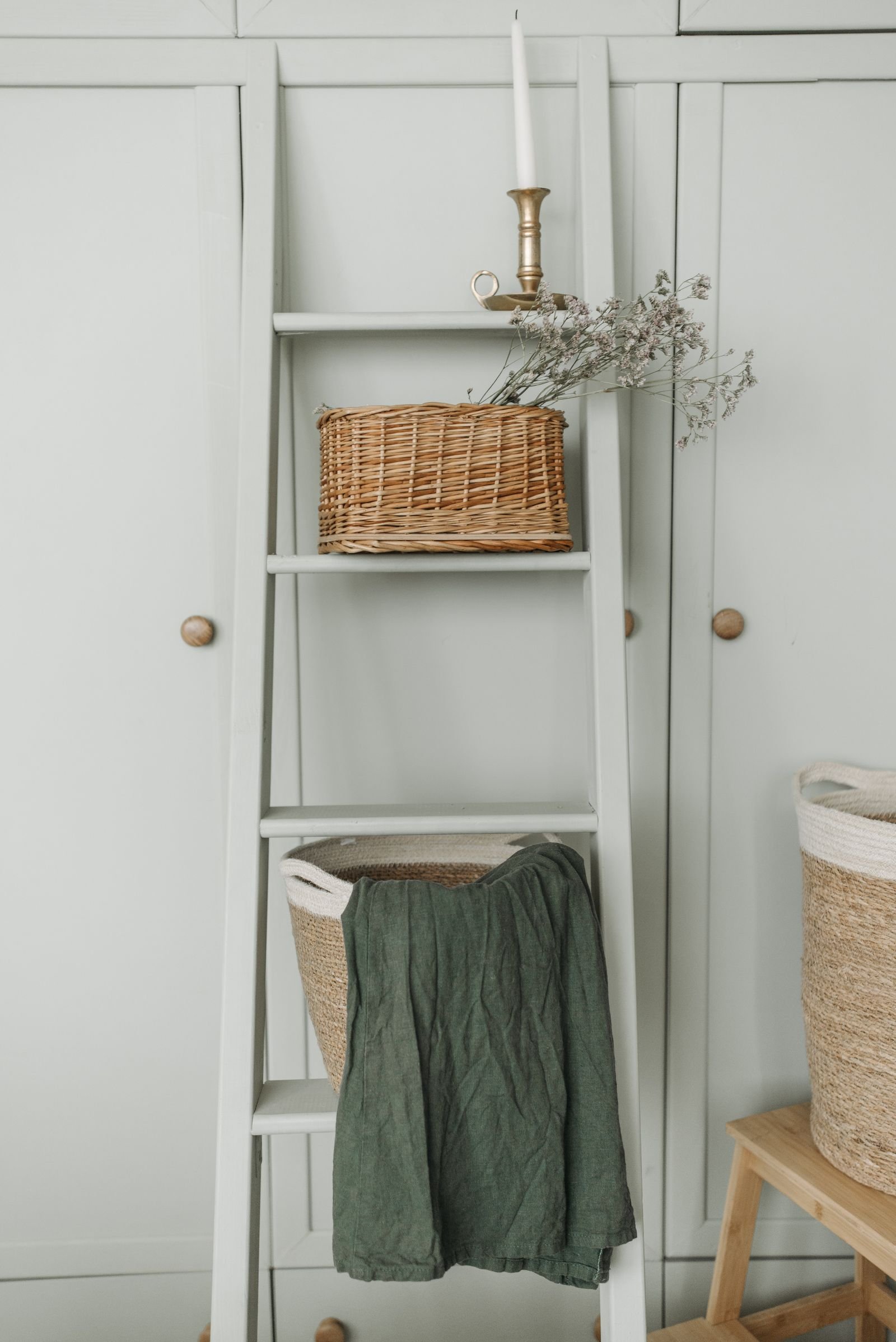 Wicker baskets on a decorative ladder next to a candle.