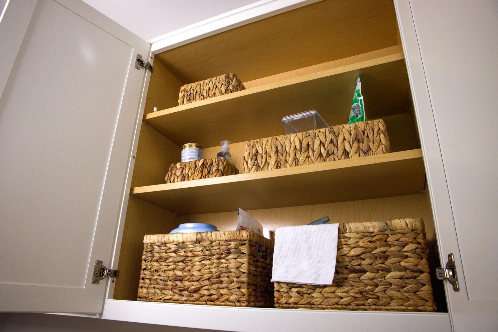 Kitchen cabinet neatly organized with wicker baskets.