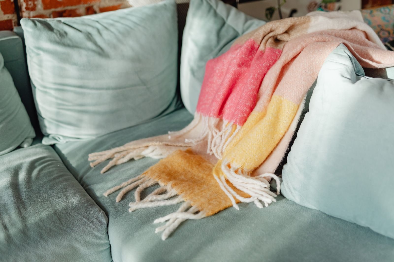 Colorful knit blanket draped over a teal living room sofa