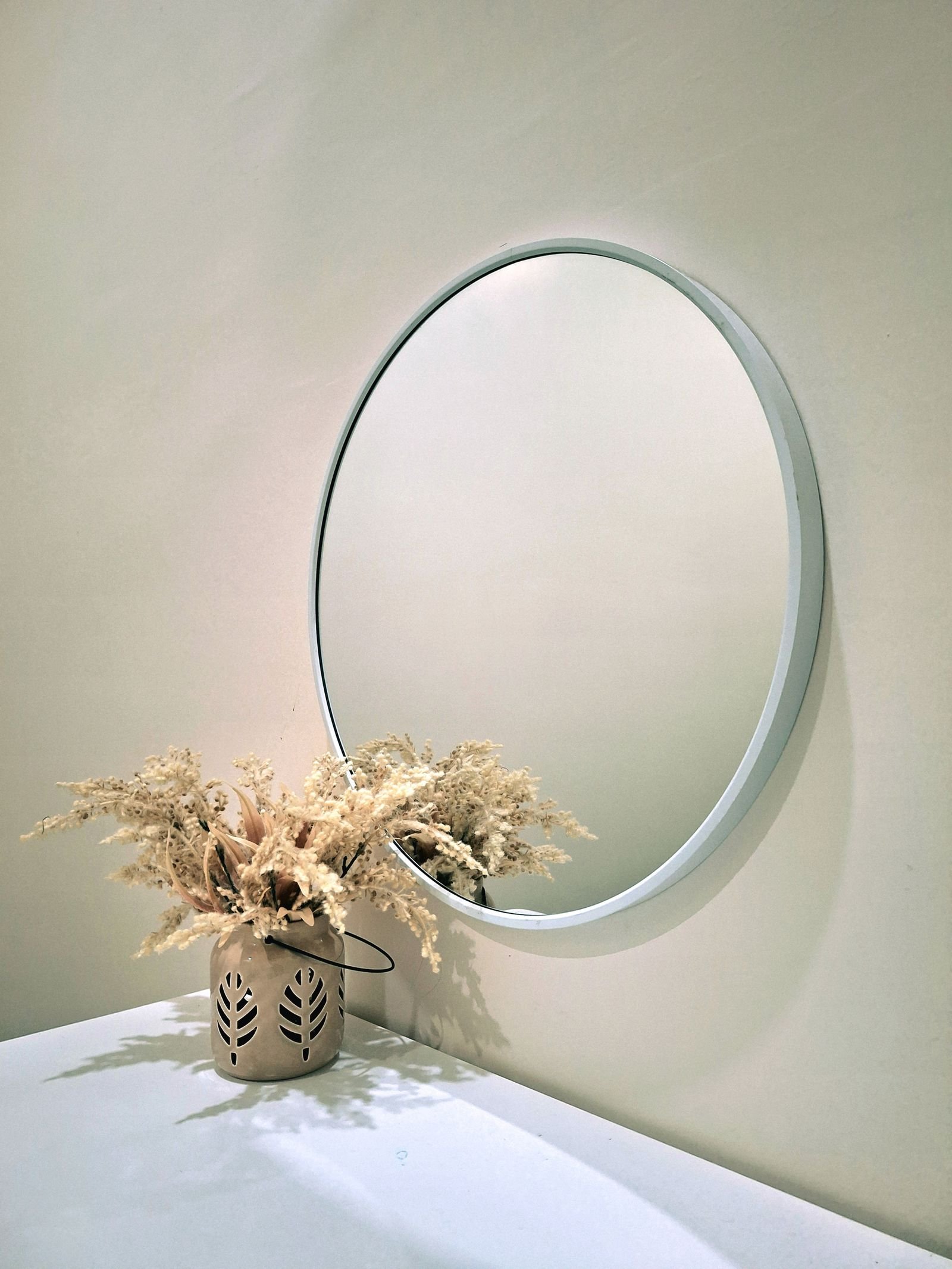 Round mirror and a decorative vase on a white surface in a minimalist interior.