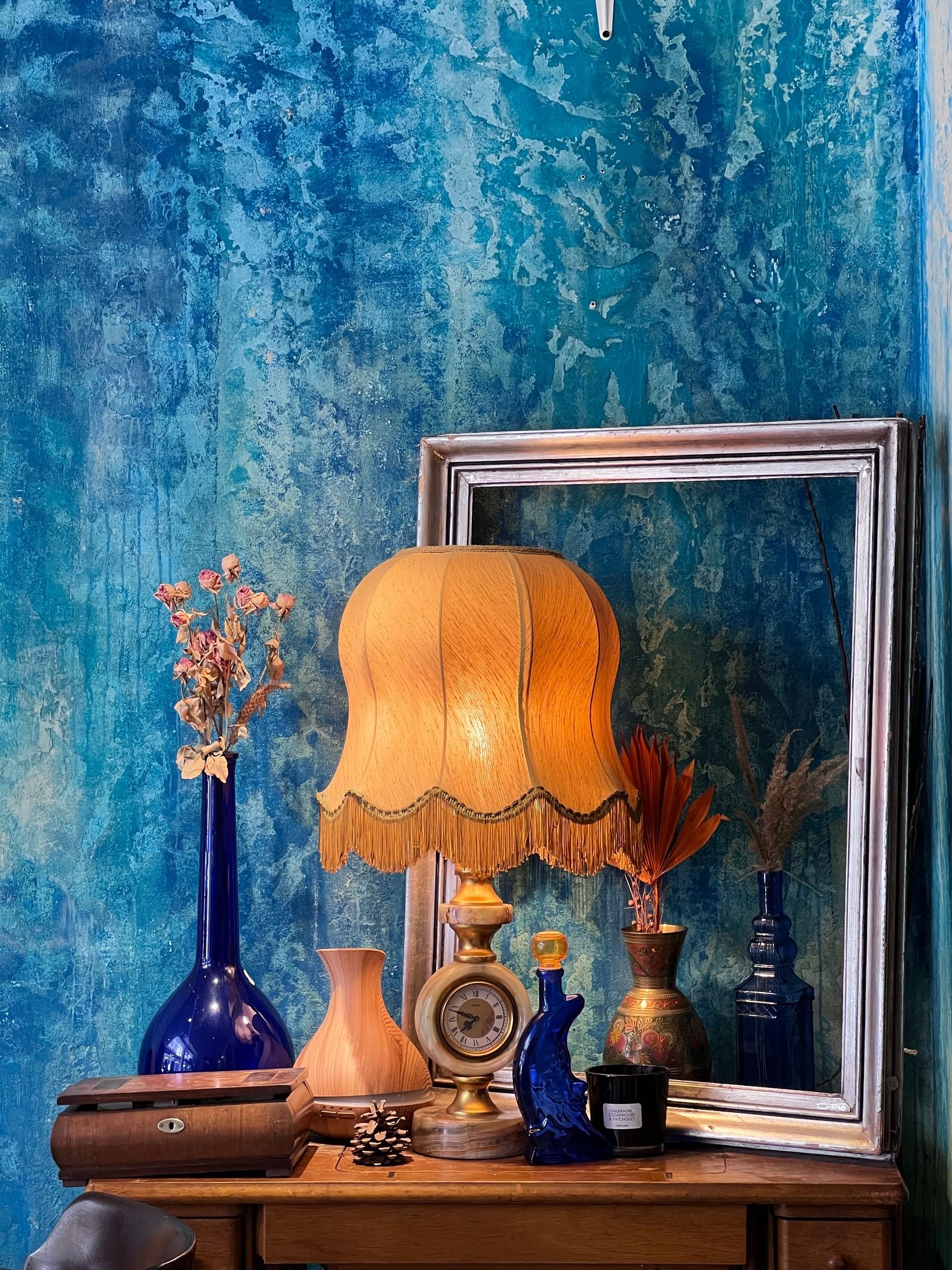 Vintage lamp, vases and a mirror against a blue wall.