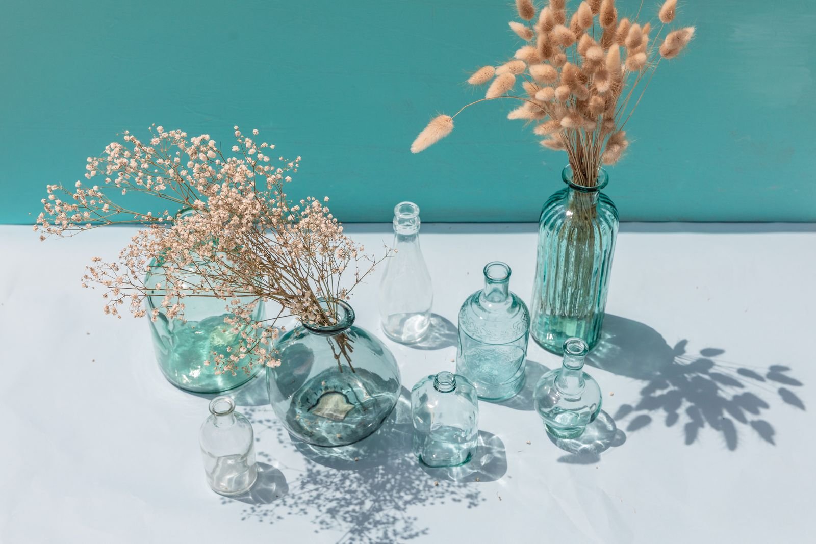 Cleaned glass bottles used as vases with dried flowers in sunlight.