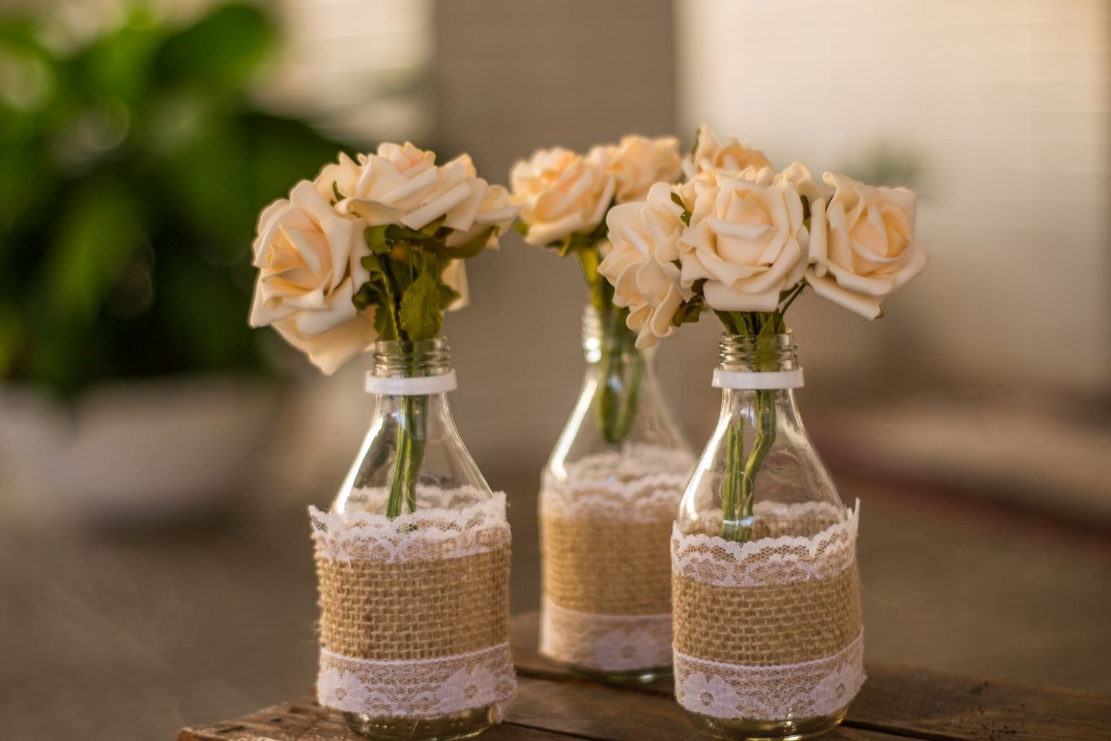 Cream roses in lace-wrapped bottles on a rustic table.