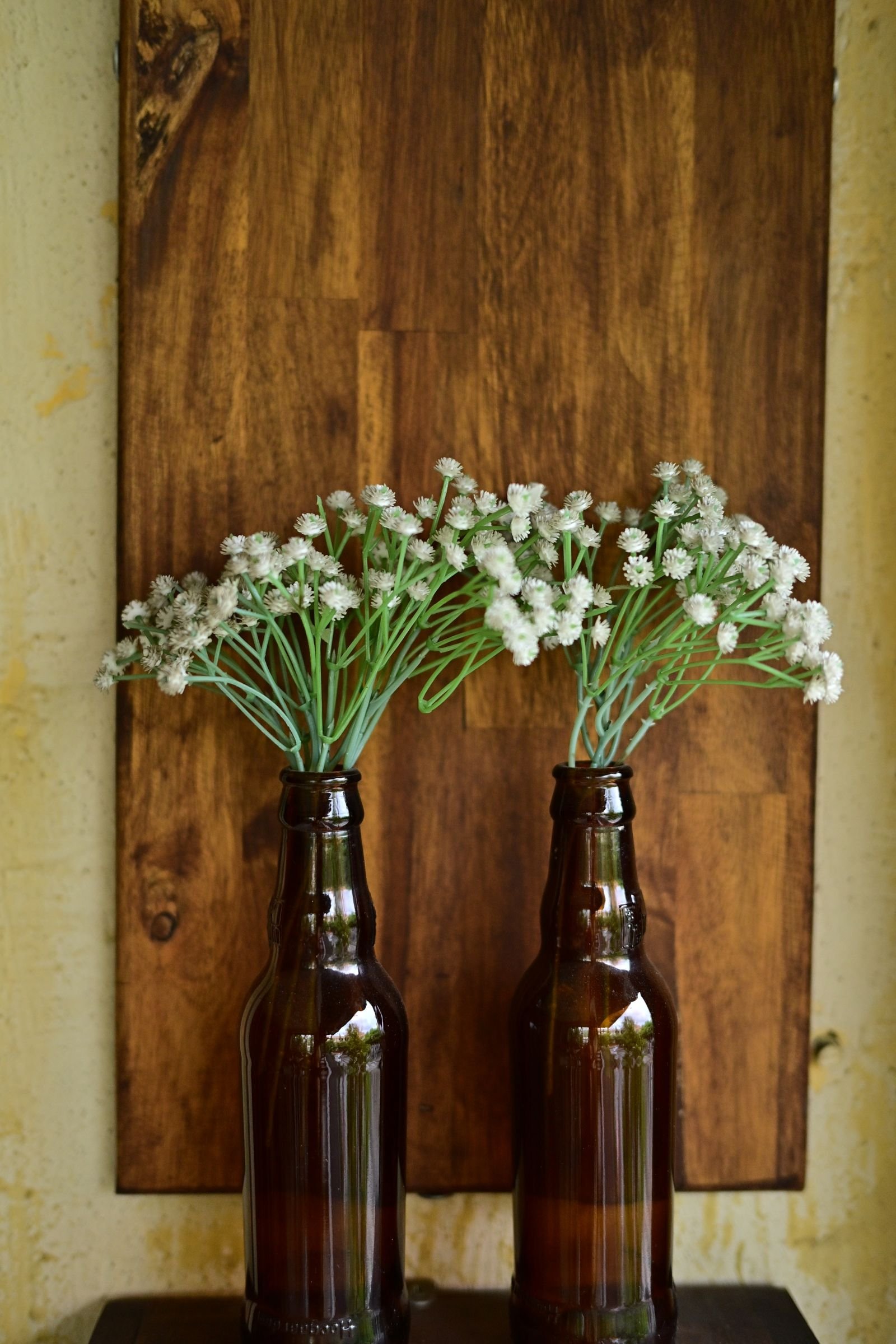 Two brown bottles holding white wildflowers on a wooden surface.