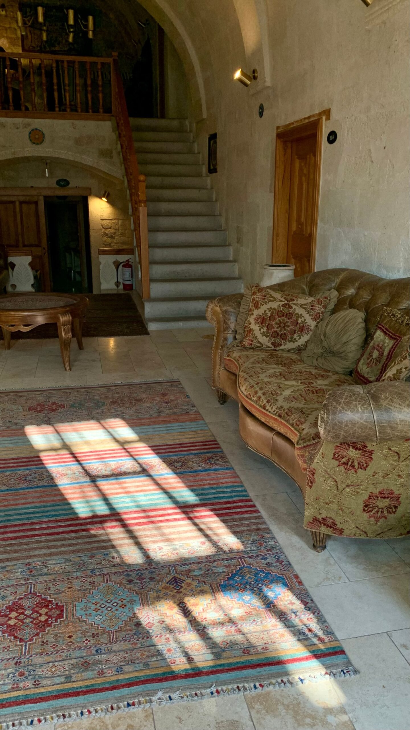 Sunlit traditional living room with a patterned rug and a vintage sofa.