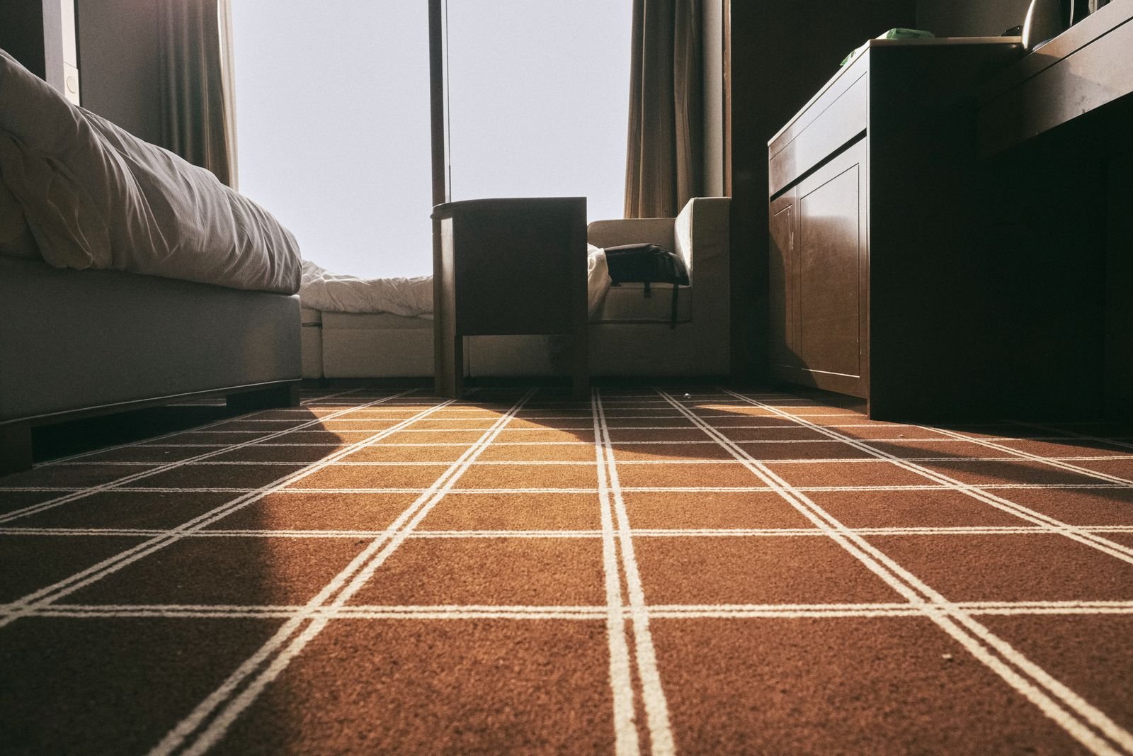 Sunlit bedroom with a patterned brown carpet and modern furniture.