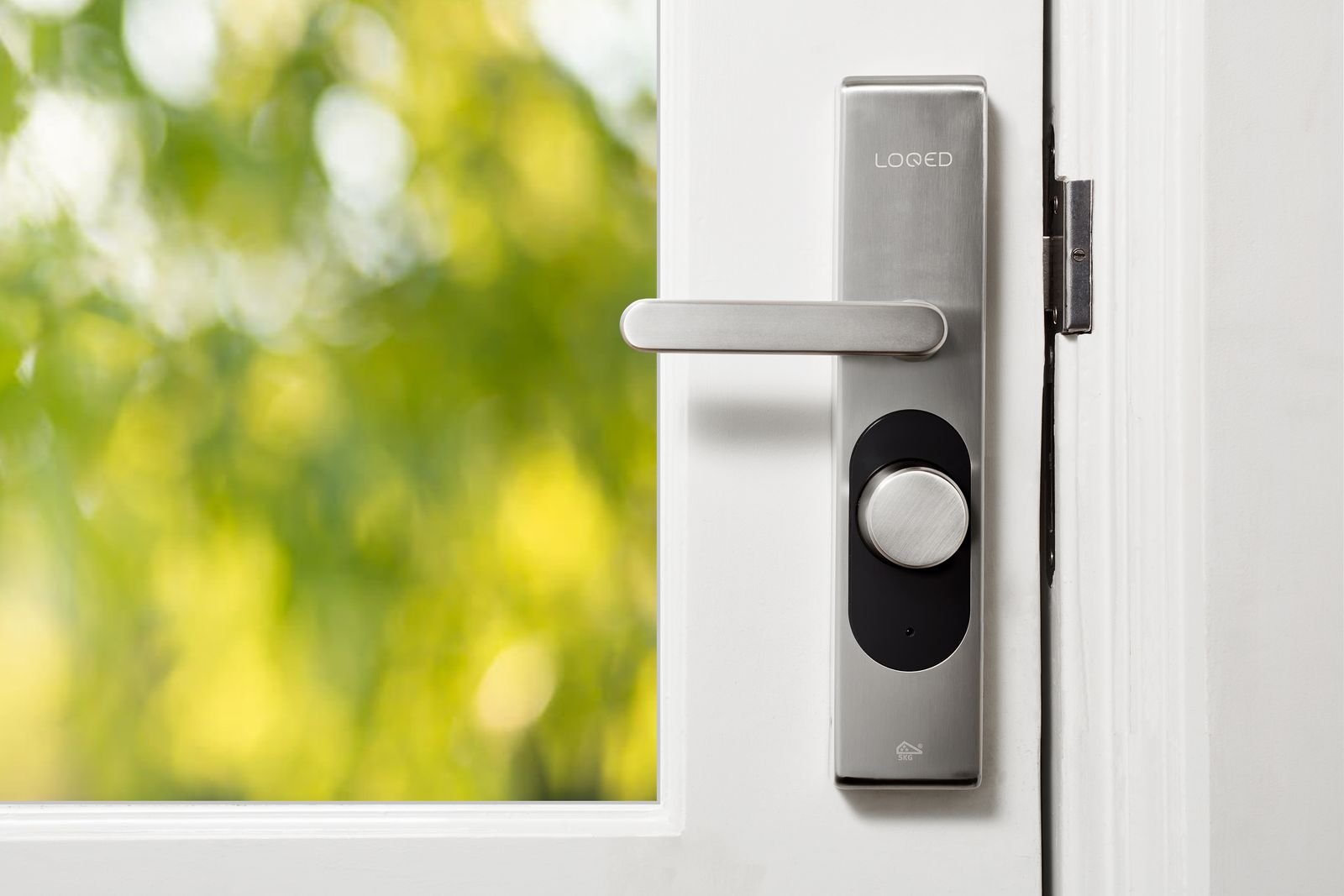 Smart door lock on a white front door with green foliage behind it