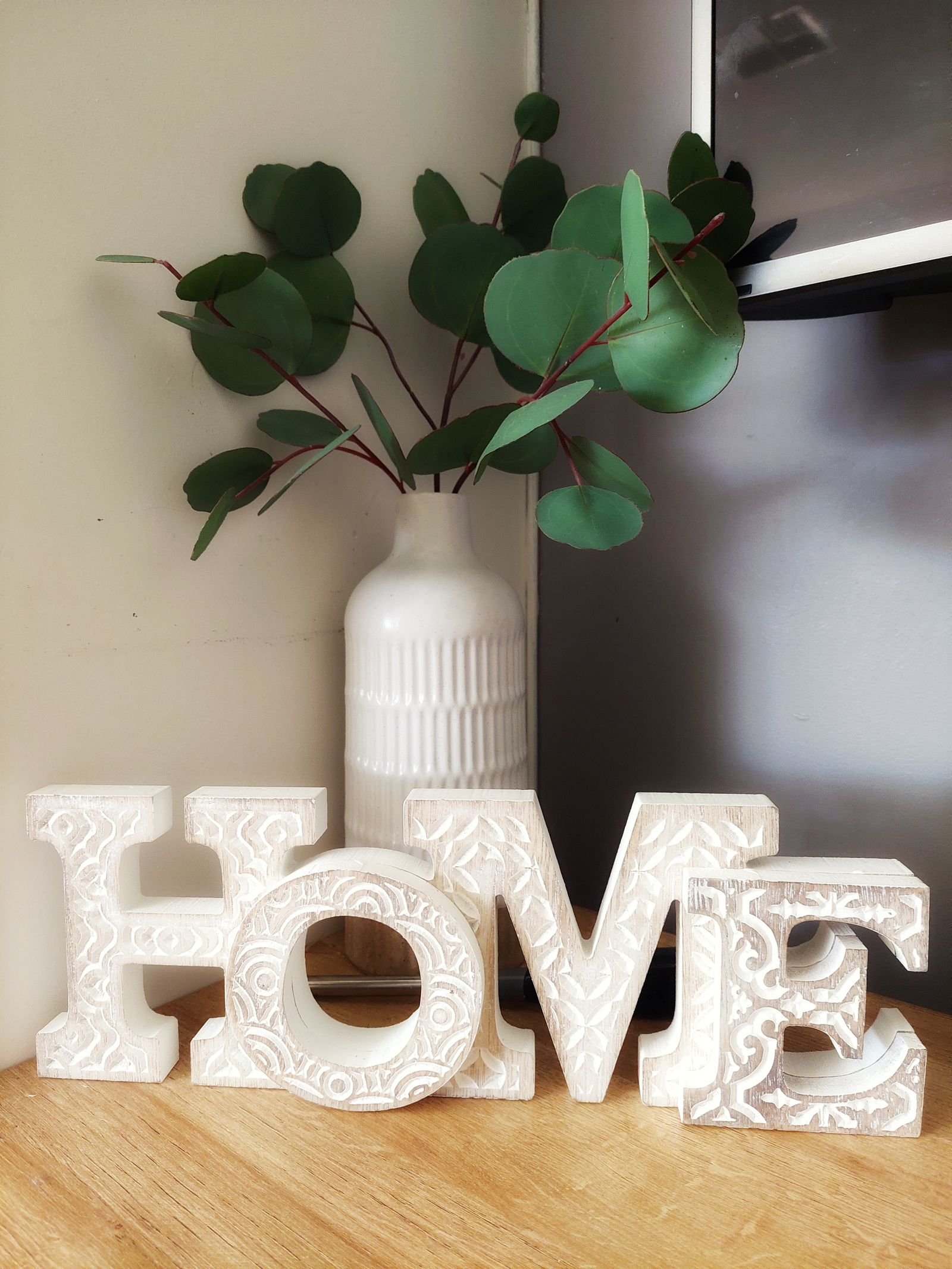 Decorative white wooden letters beside a ceramic vase with green leaves