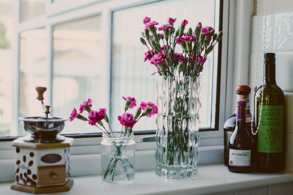 A stylish kitchen scene with flowers in vases beside wine bottles on a windowsill.