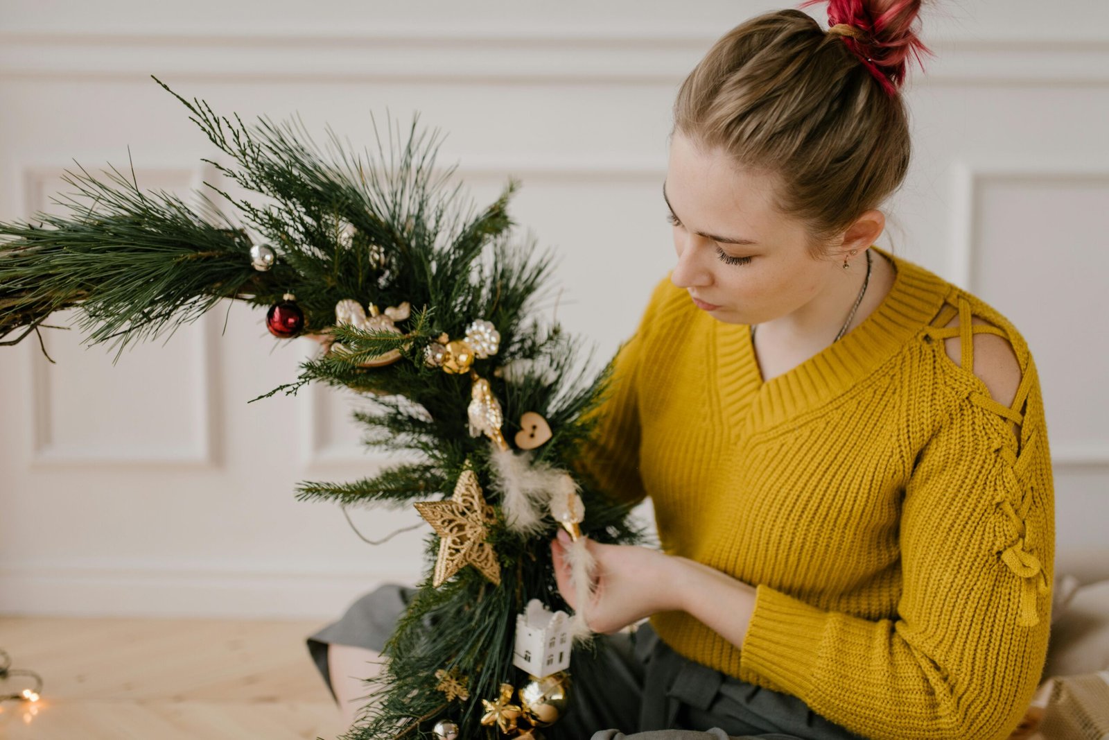A woman carefully decorates a festive Christmas wreath indoors.