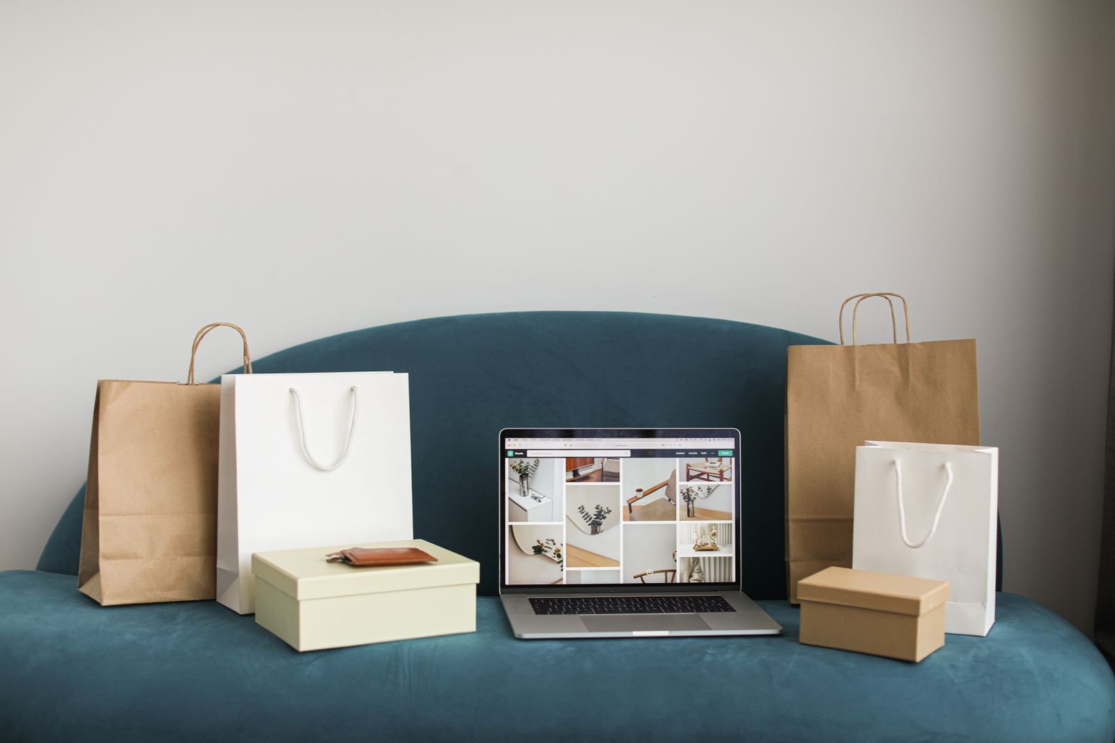 Laptop with shopping bags and boxes on a blue sofa after shopping online for home decor deals
