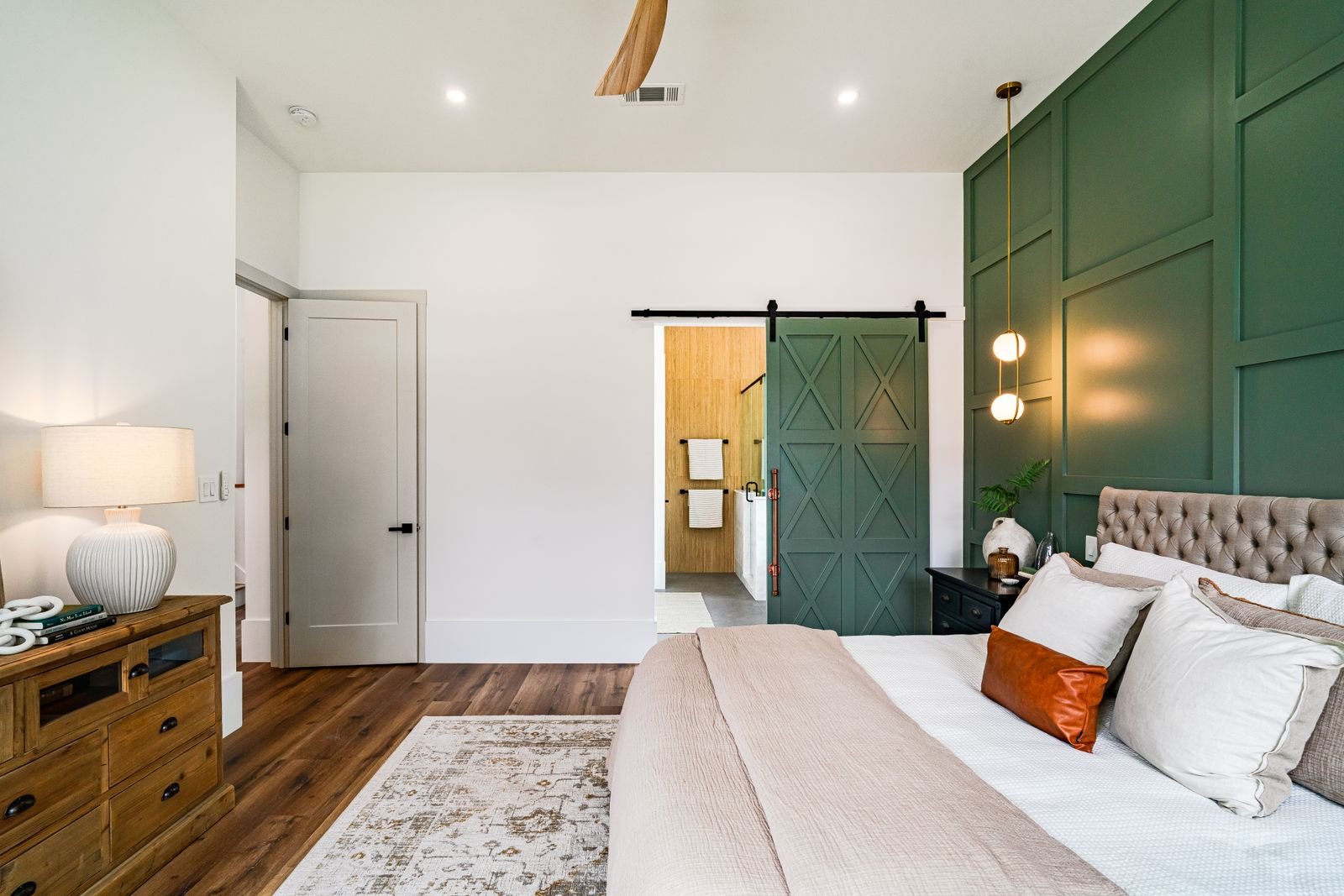 Modern bedroom with a green accent wall and a barn door leading to the bathroom.